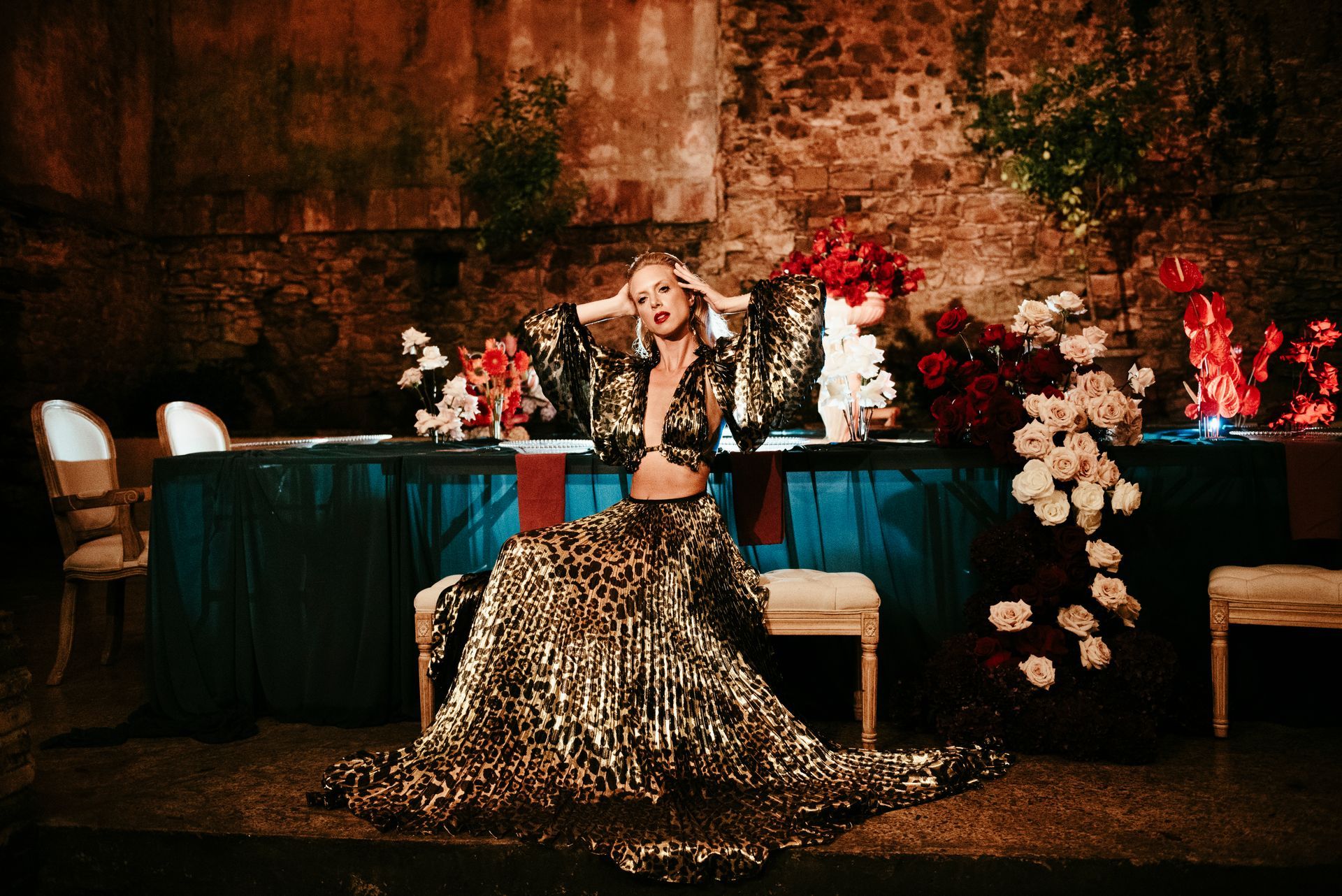 Woman in leopard print outfit poses at a table with flowers. Outdoor setting, warm lighting.