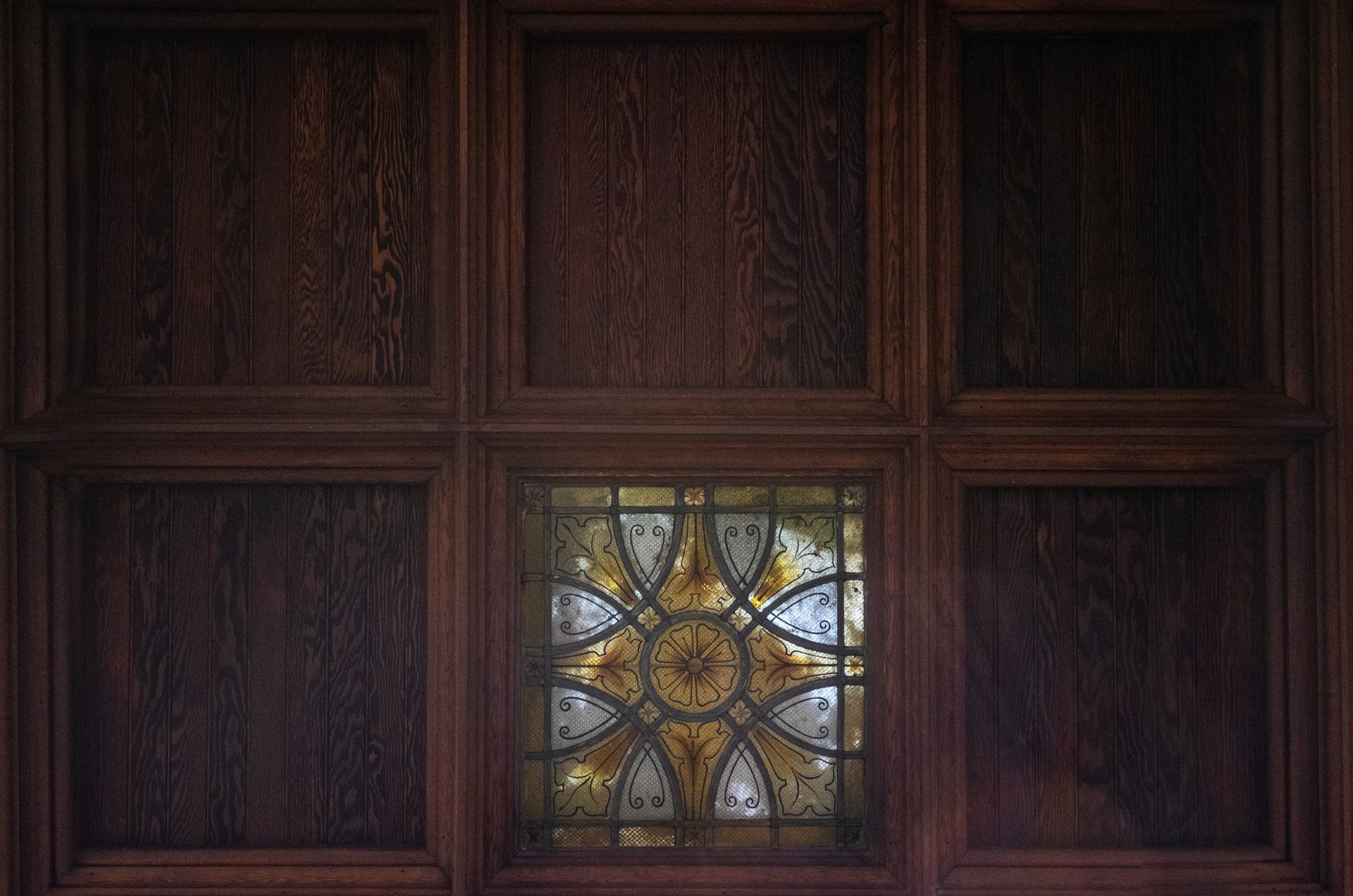 There is a stained glass window in the middle of a wooden wall.
