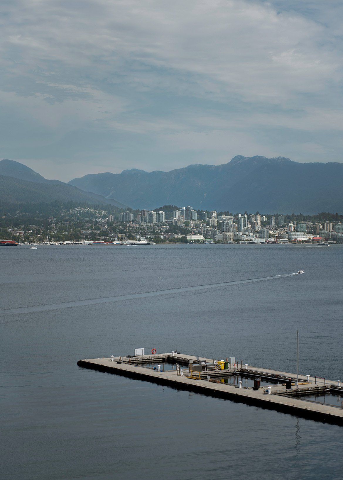 Dock on water with city and mountains in the background under a cloudy sky.