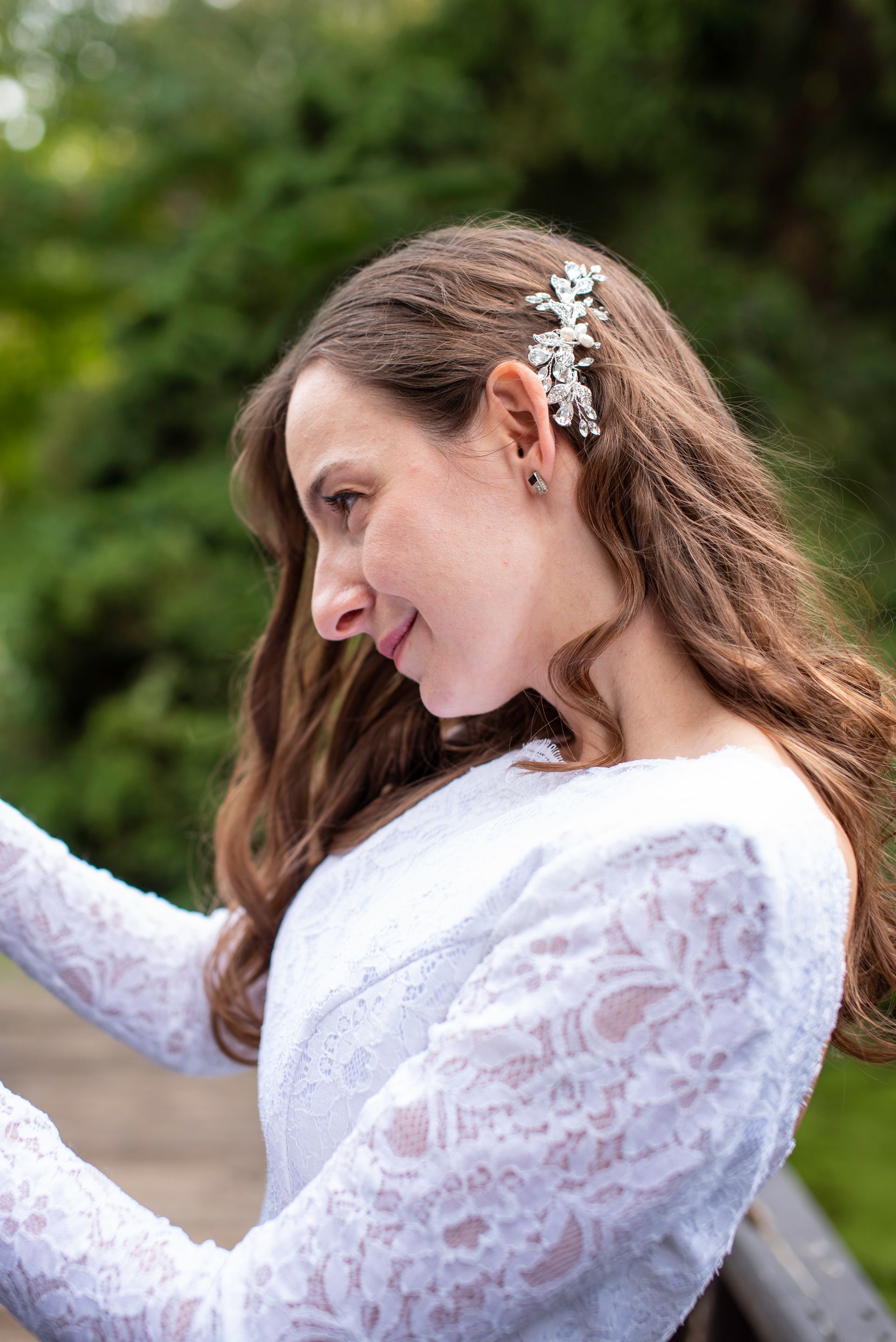 Woman with long brown hair wearing a white lace dress, looking down with a decorative hair clip.