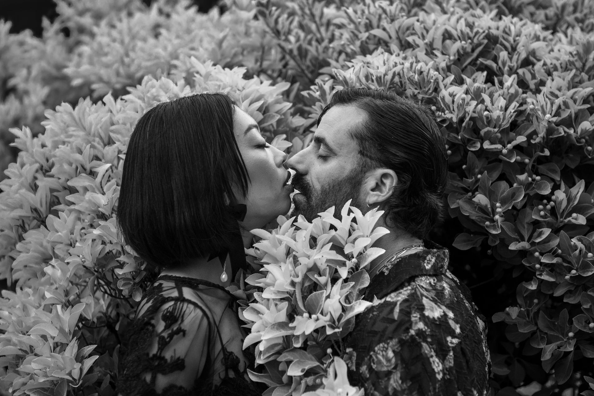 Couple kissing amidst lush foliage. Black and white photo.
