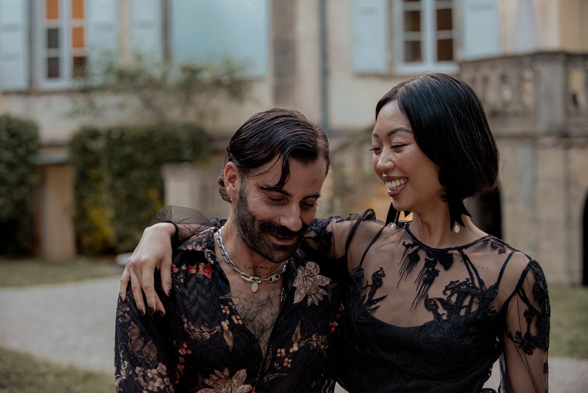 Man with wet hair and woman with arm around him smiling, outdoors.