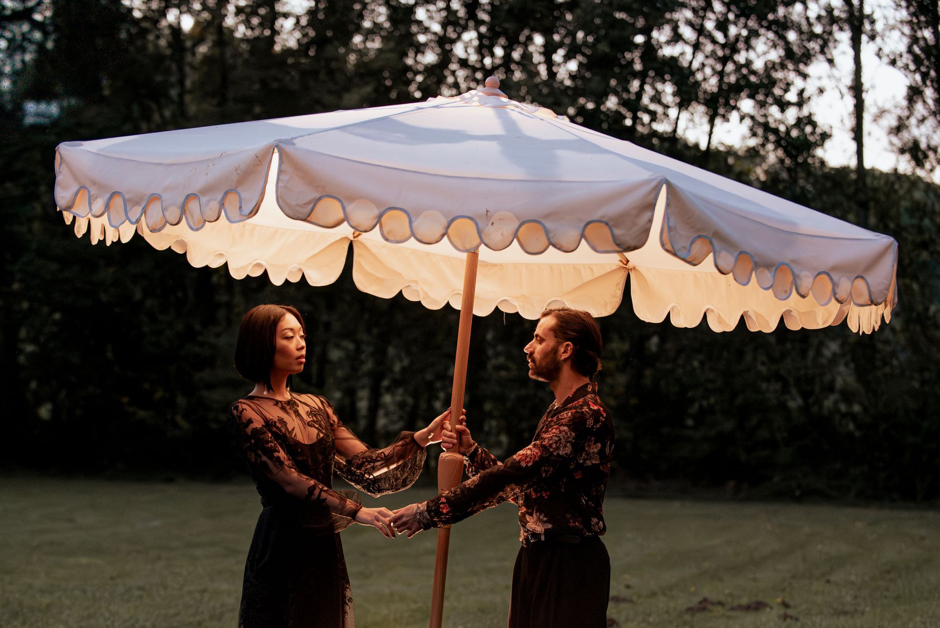 Couple holding hands under a scalloped parasol in a grassy area.