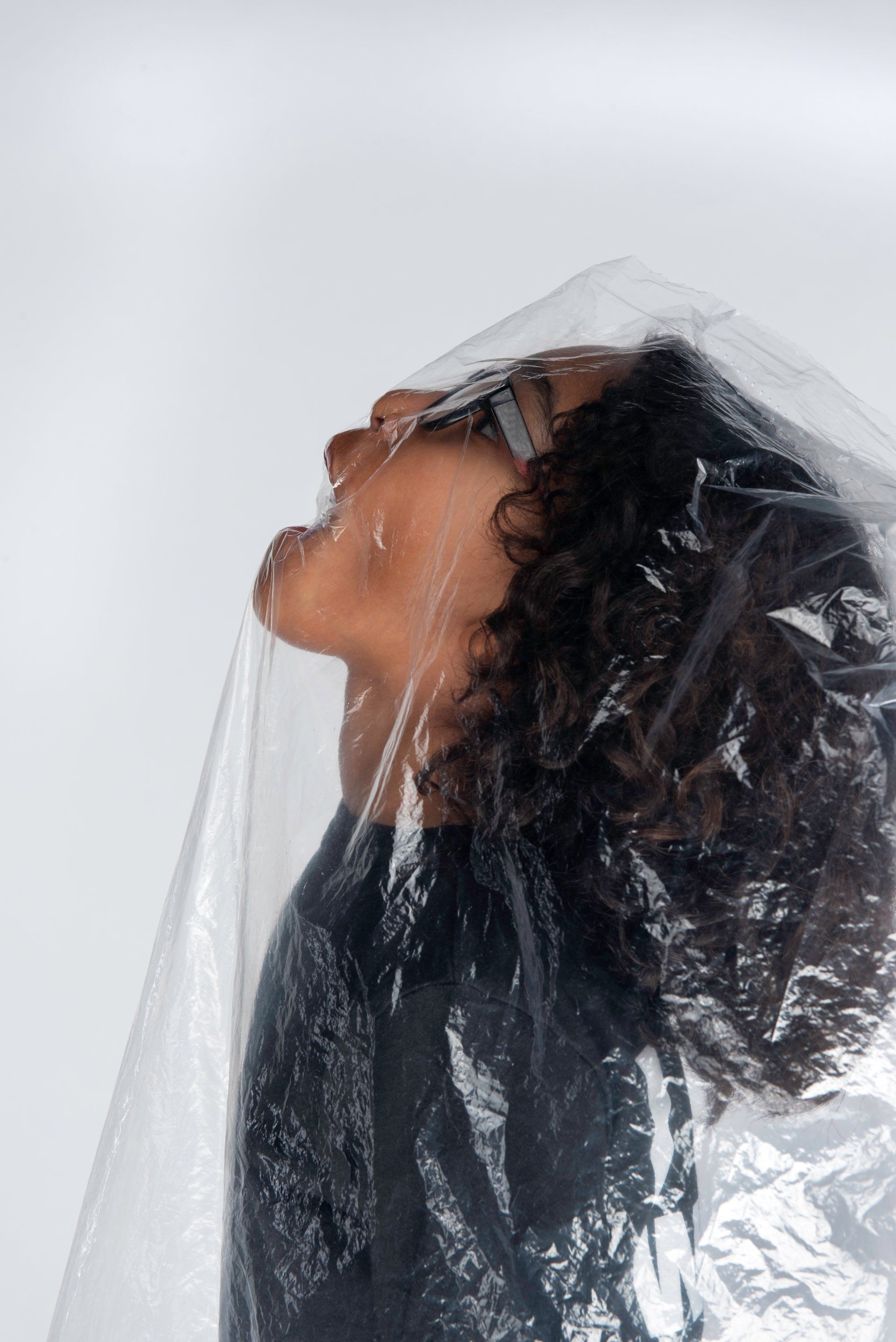 Person's face partially covered by clear plastic, looking up with open mouth; neutral background.