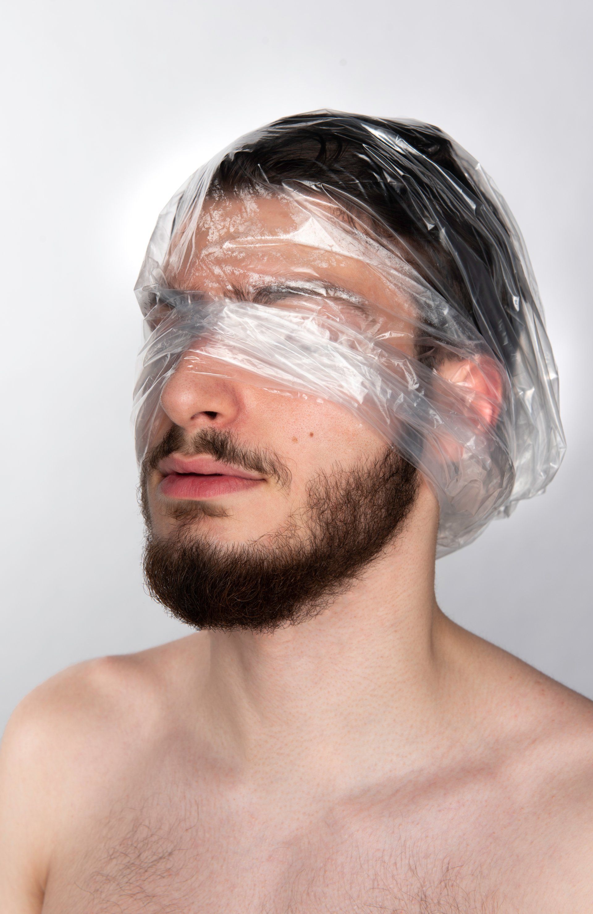 Man with eyes and head covered in clear plastic wrap, against a white background.