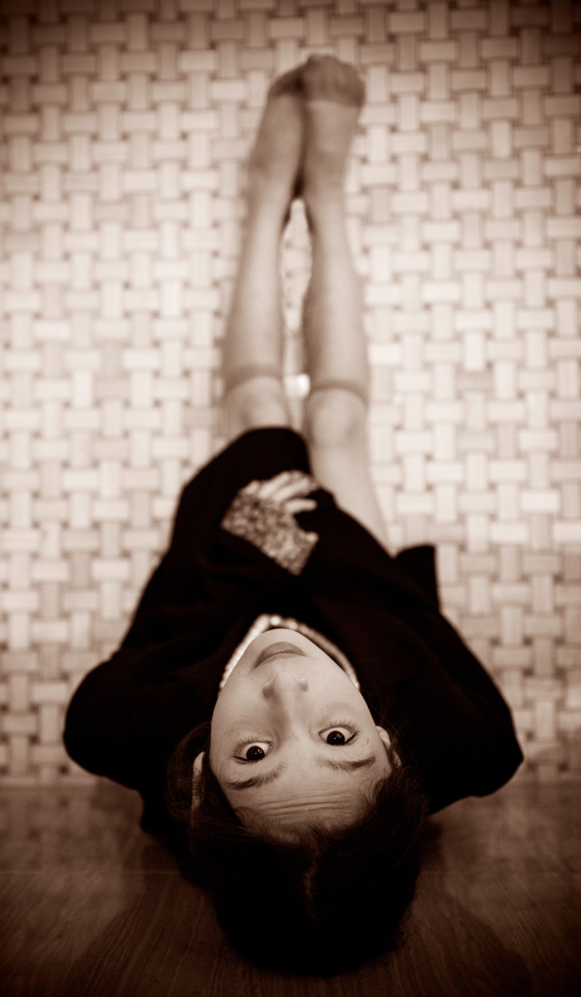 Girl lying on back, legs up, looking upwards, on woven surface. Sepia tone.