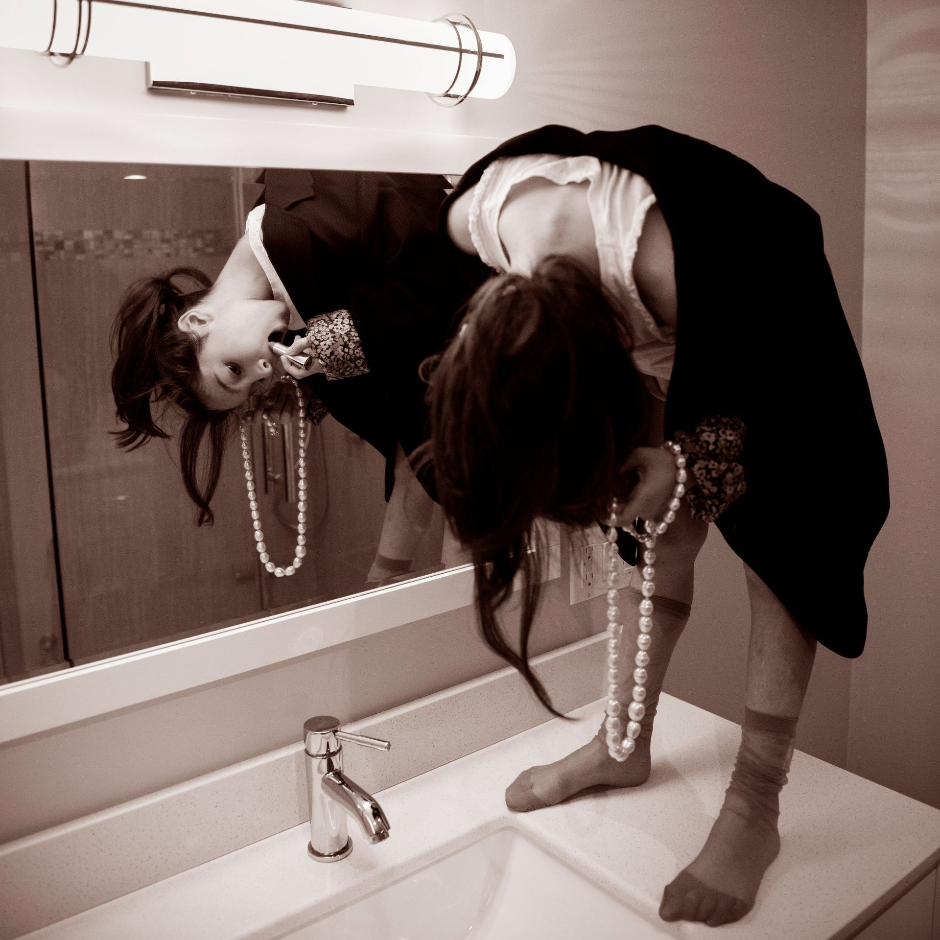 A girl sitting on a counter in front of a mirror.