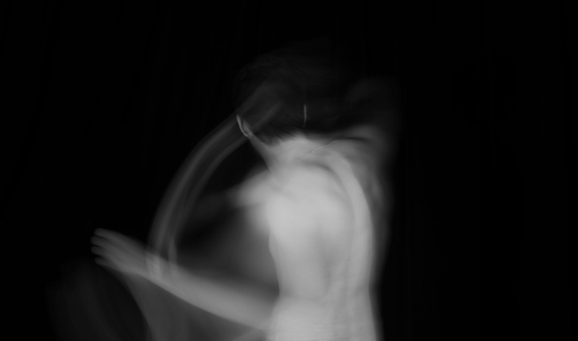 A blurry black and white photo of a man dancing in the dark.