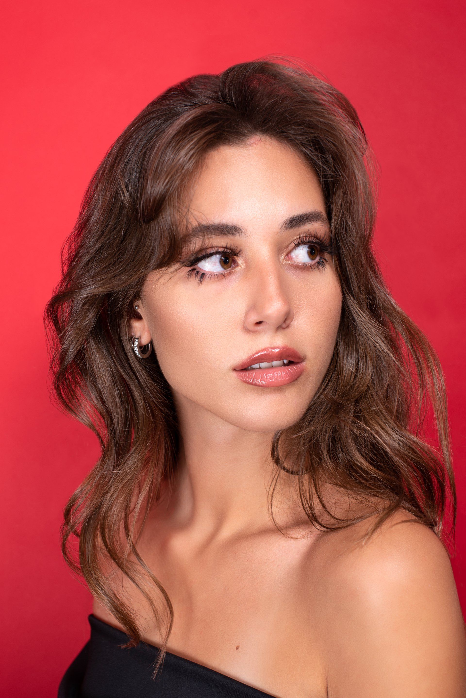 Woman with brown wavy hair looking to the side, red background.