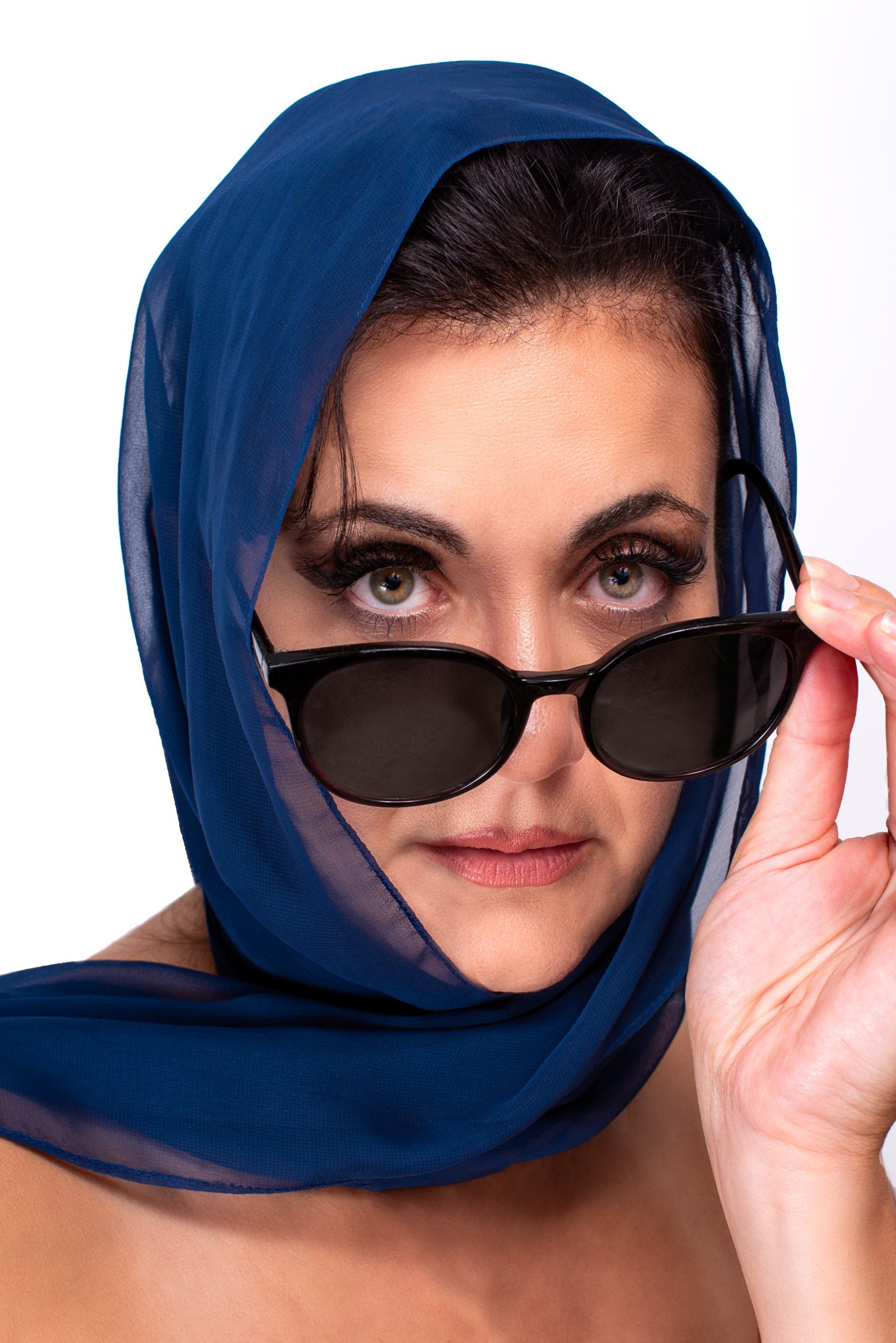 Woman wearing a blue scarf and sunglasses, looking over the glasses with a serious expression.