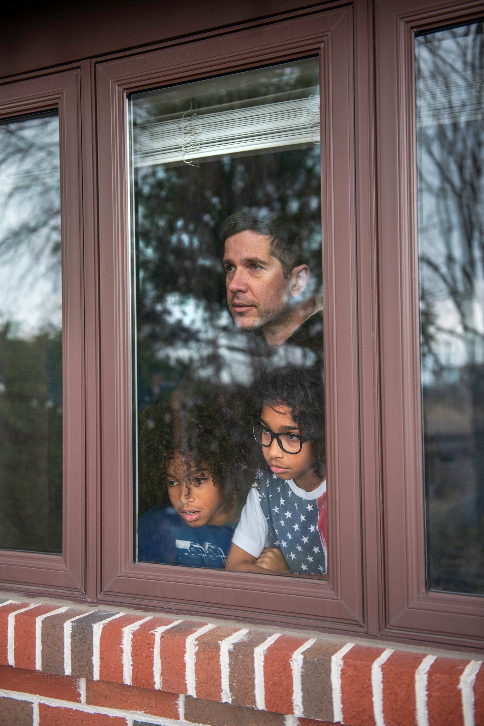 A man and two children are looking out of a window.