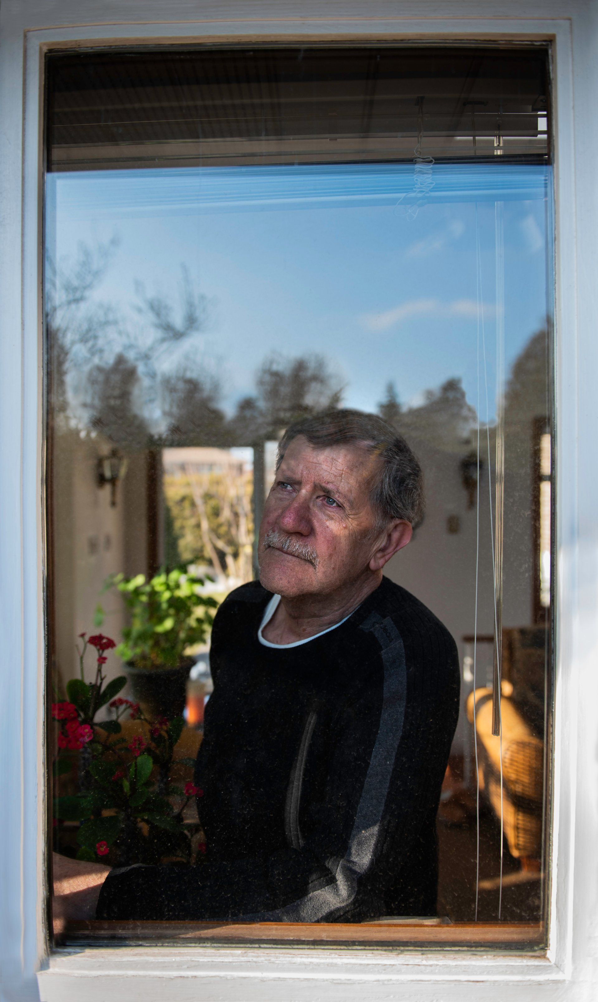 An elderly man is looking out of a window.