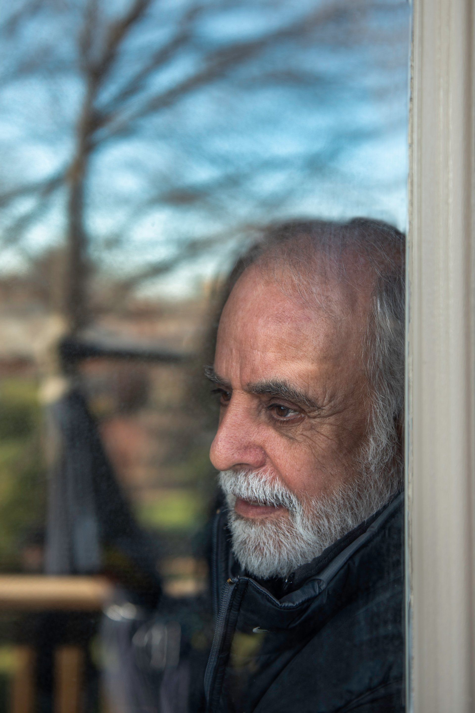 A man with a beard is looking out of a window.