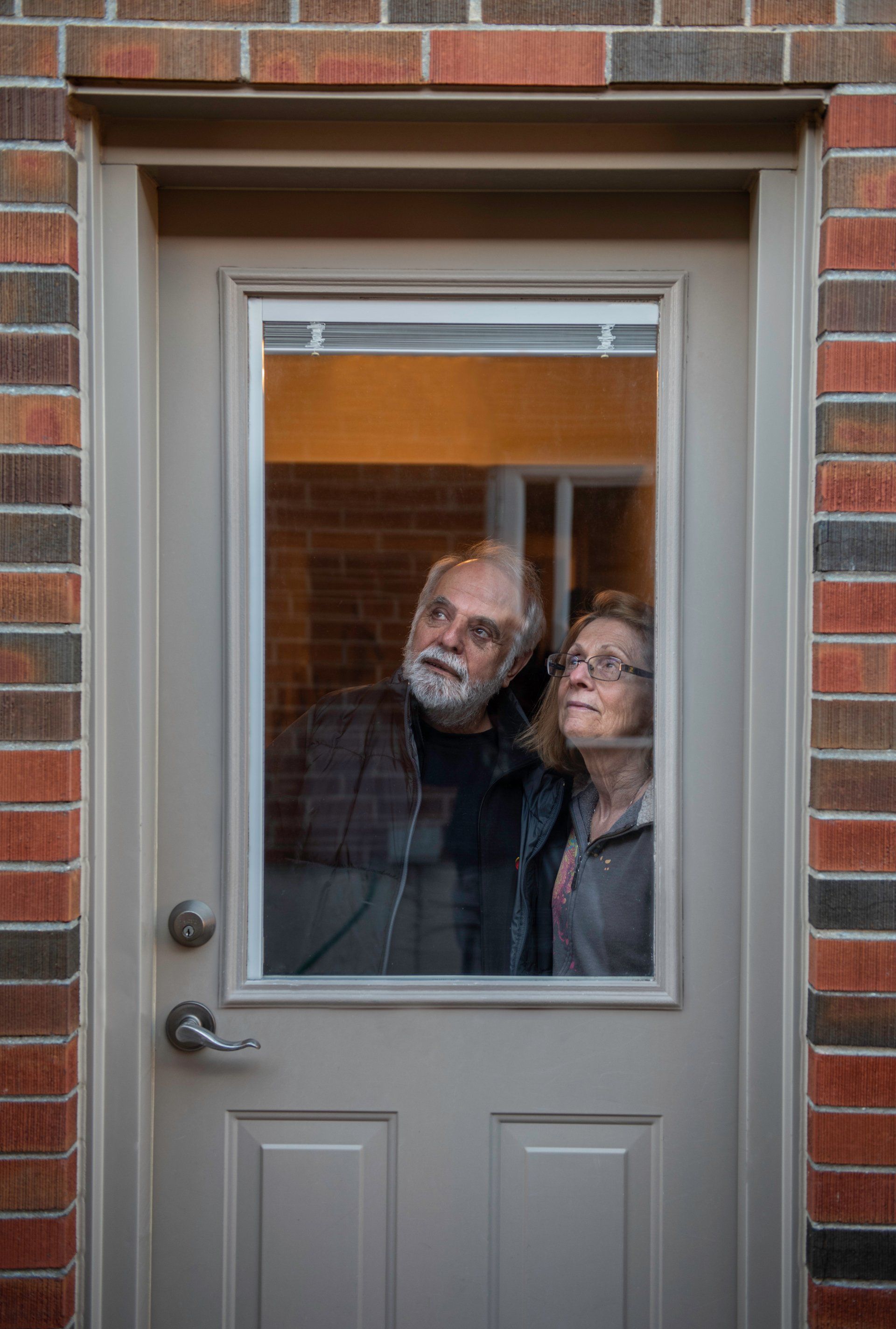 A man and a woman are looking out of a door.