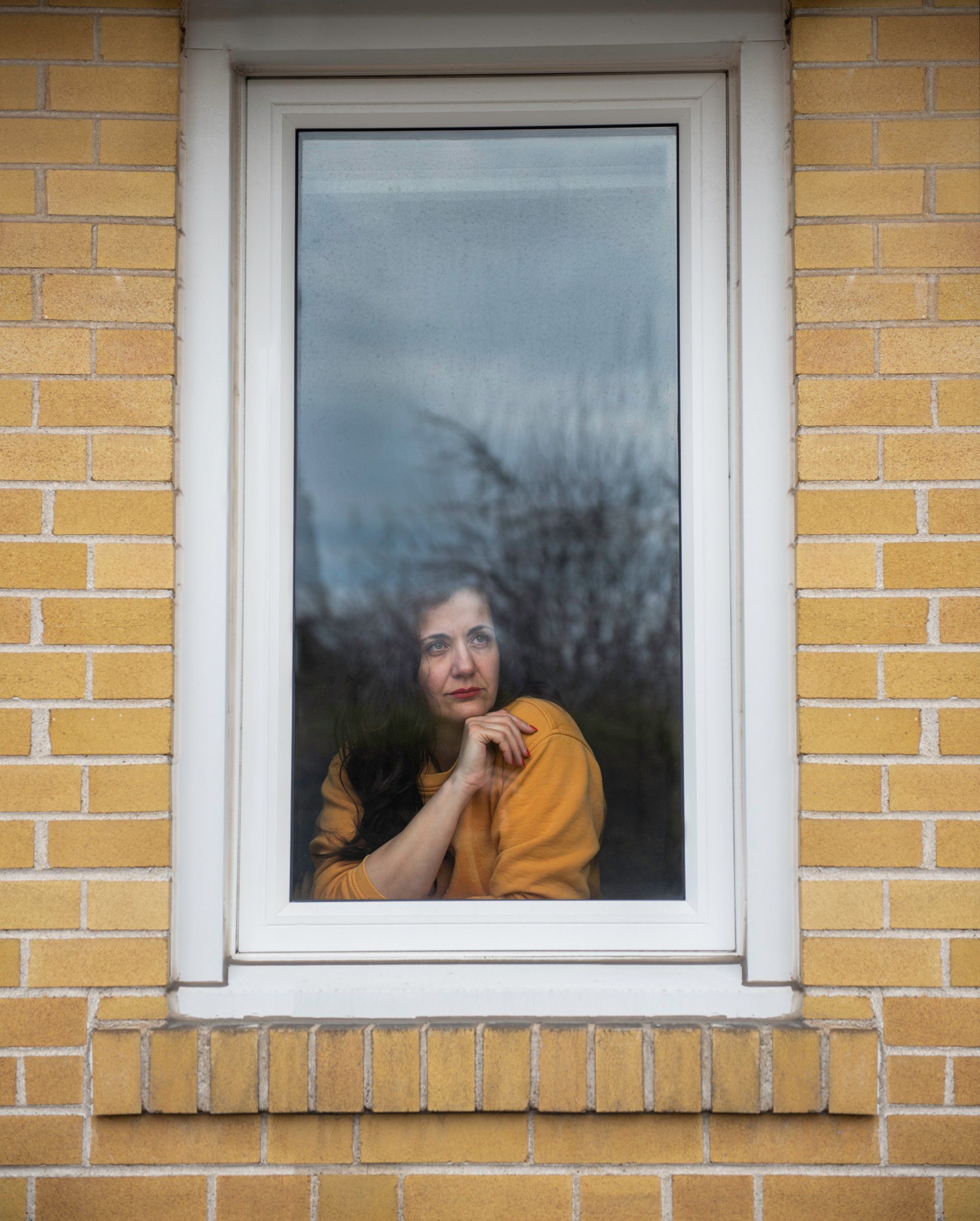 A woman is looking out of a window on a brick wall.