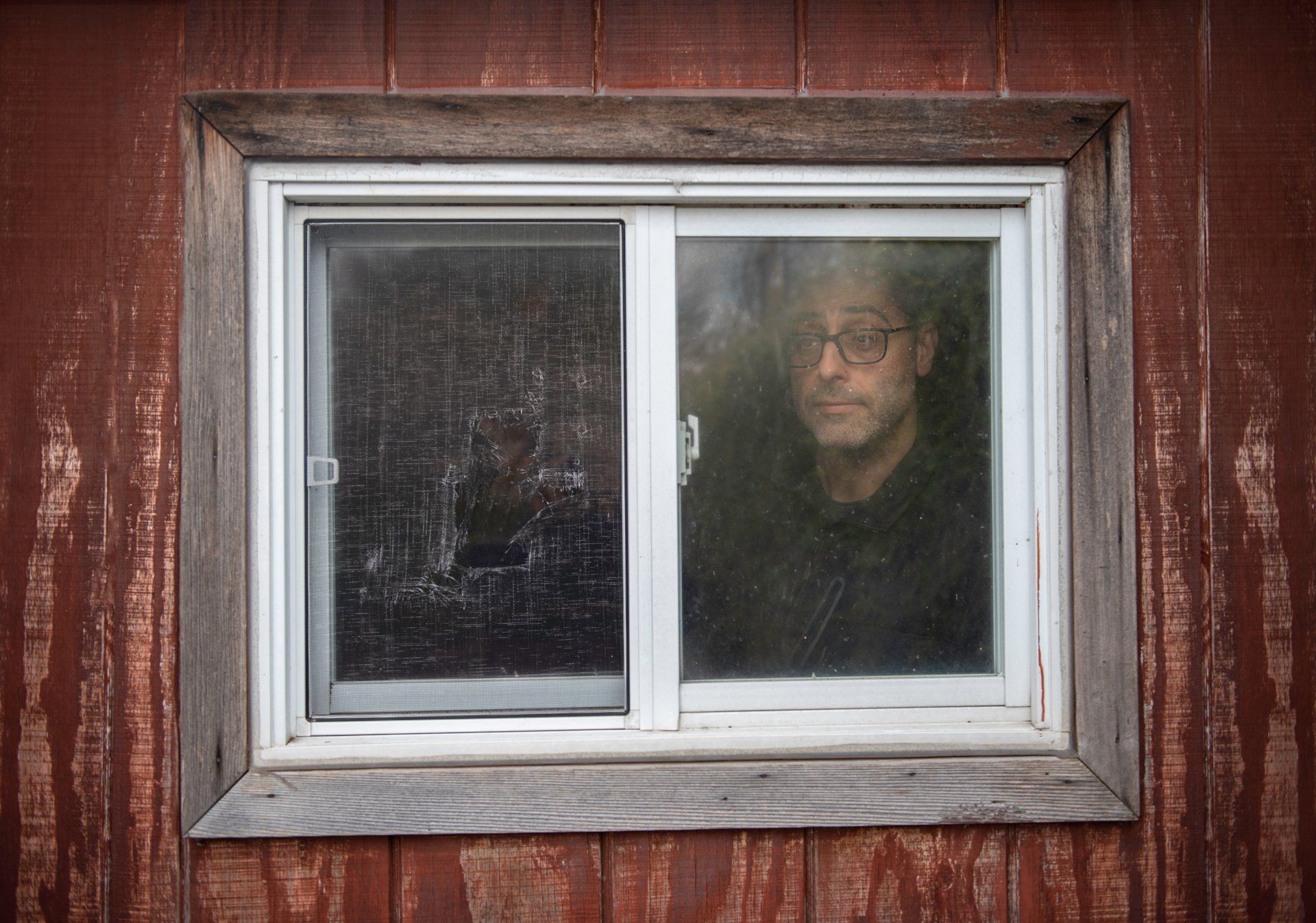 A man with glasses is looking out of a window.
