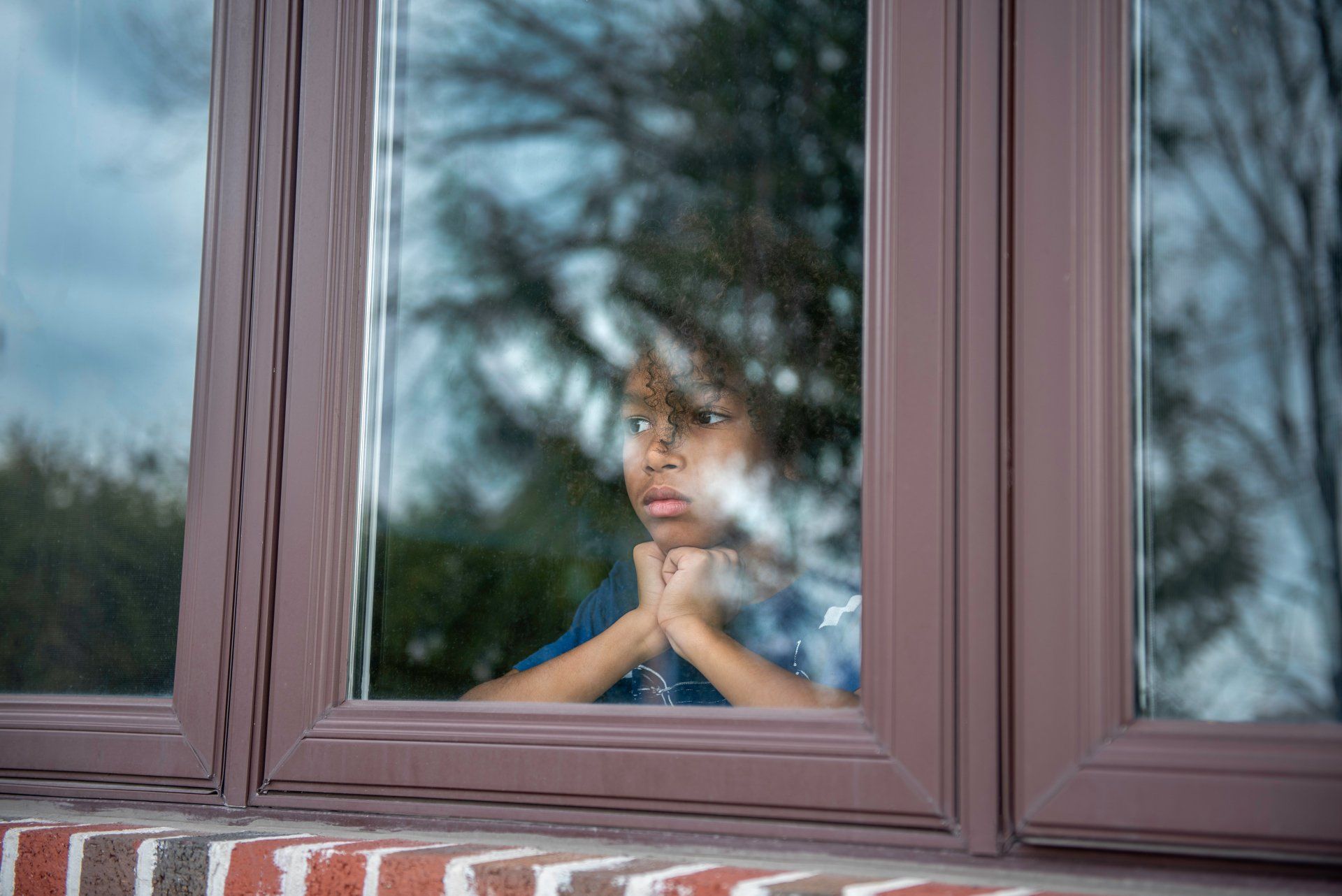 A young boy is looking out of a window.