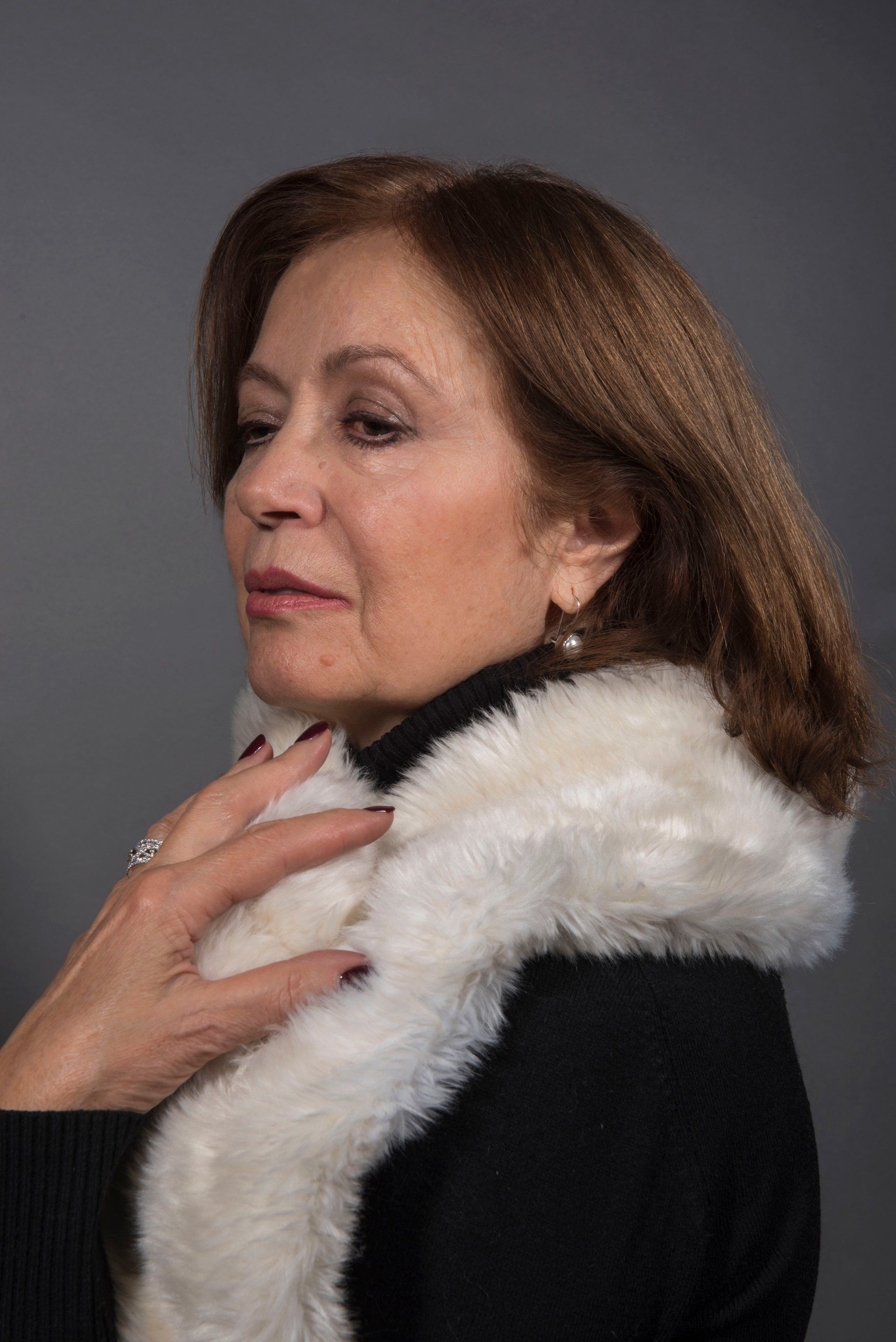 Woman wearing a black sweater and white fur scarf. Her hand rests on the scarf.