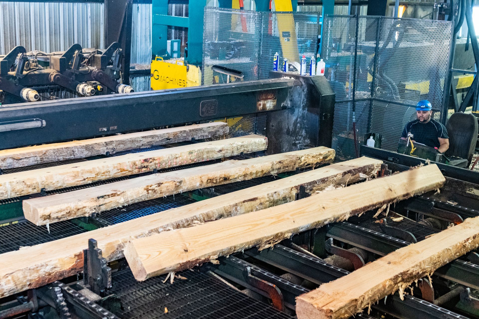 A man is working on a machine that is cutting wood in a factory.