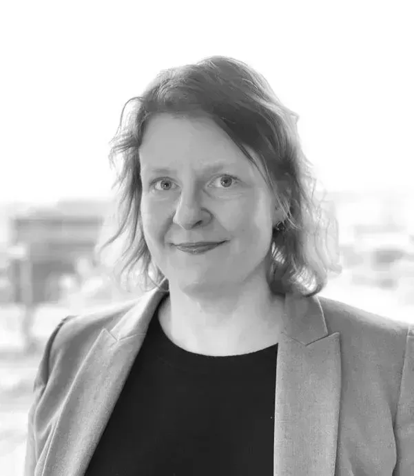 A woman in a suit and black shirt is smiling in a black and white photo.