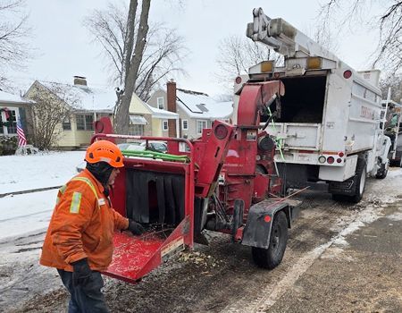 A man is standing next to a tree chipper on a snowy street.