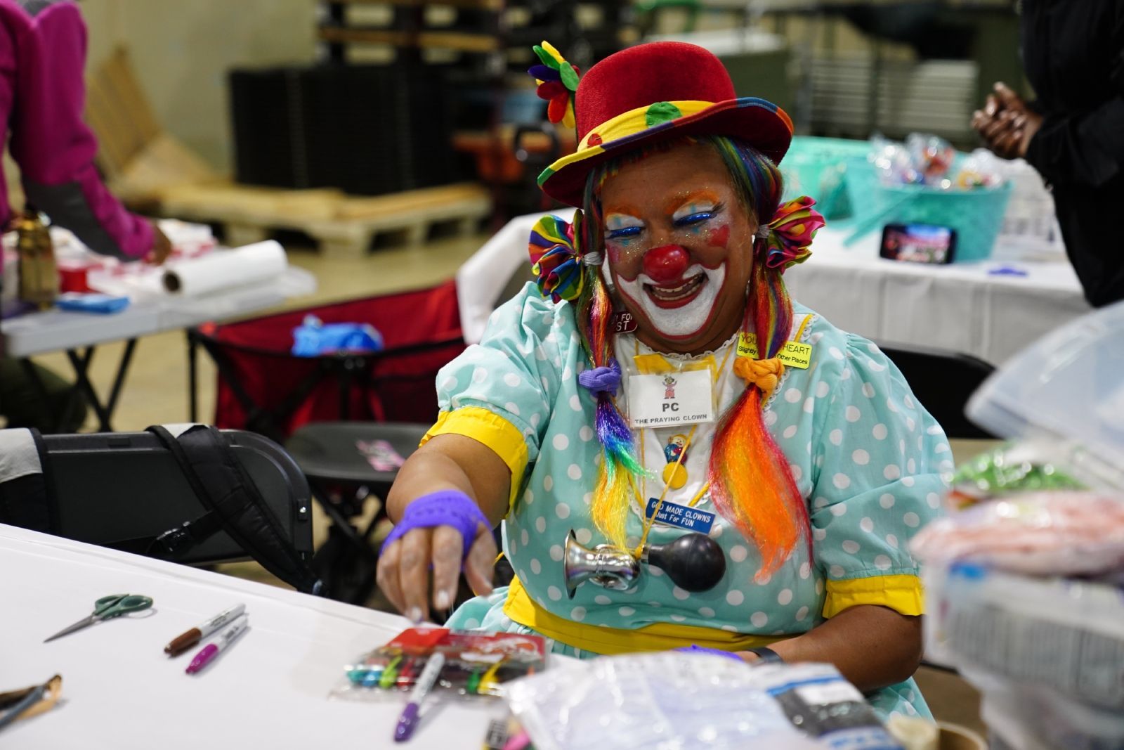 Clown in colorful costume and red hat painting at a table in a craft room