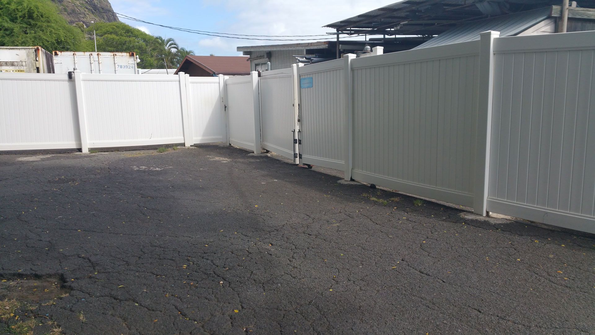 White fence enclosing a dark paved area, with buildings and a mountain in the background.