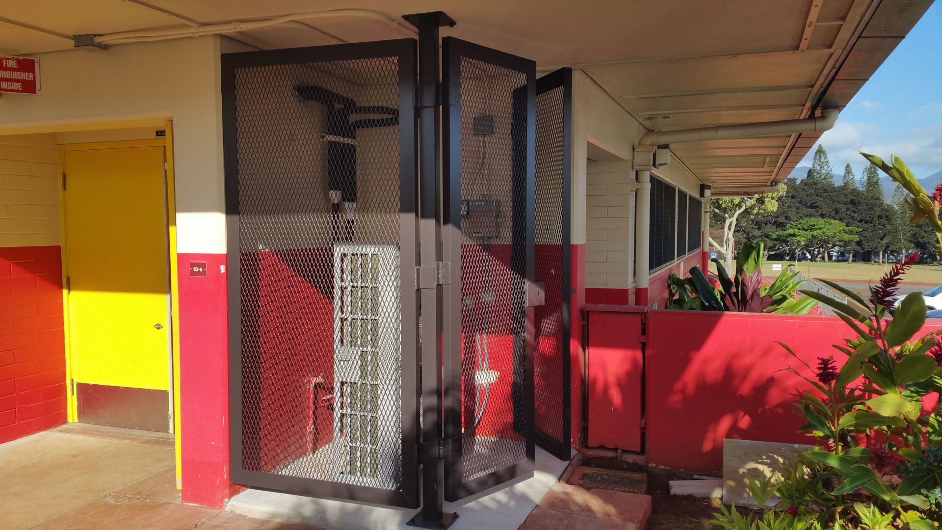 Exterior of a building with red and yellow accents, a security gate, and a doorway.