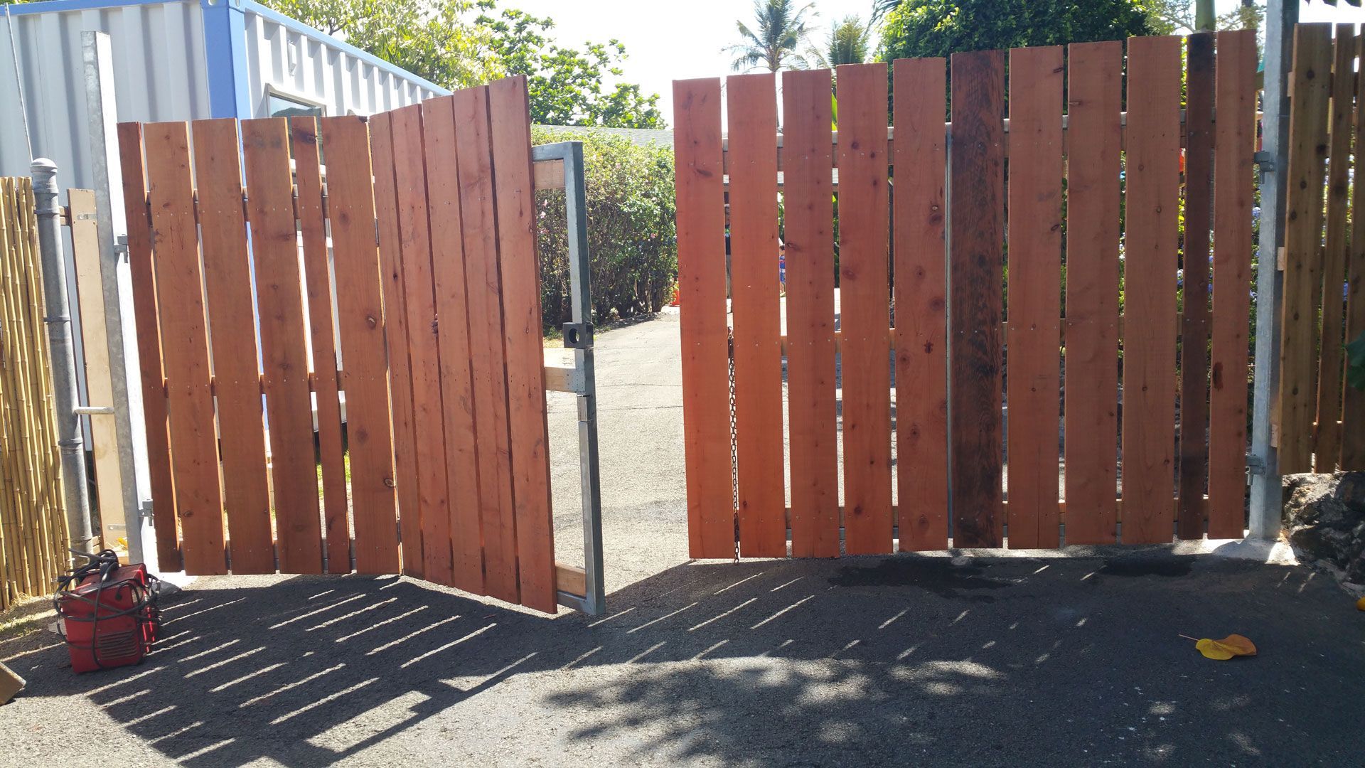 Wooden fence gate open on an asphalt drive. Brown wooden planks on metal frames.