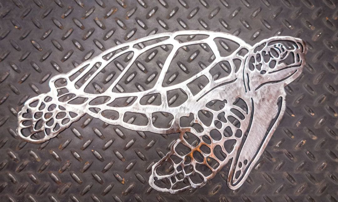 Metal cutout of a sea turtle on a textured metal surface.