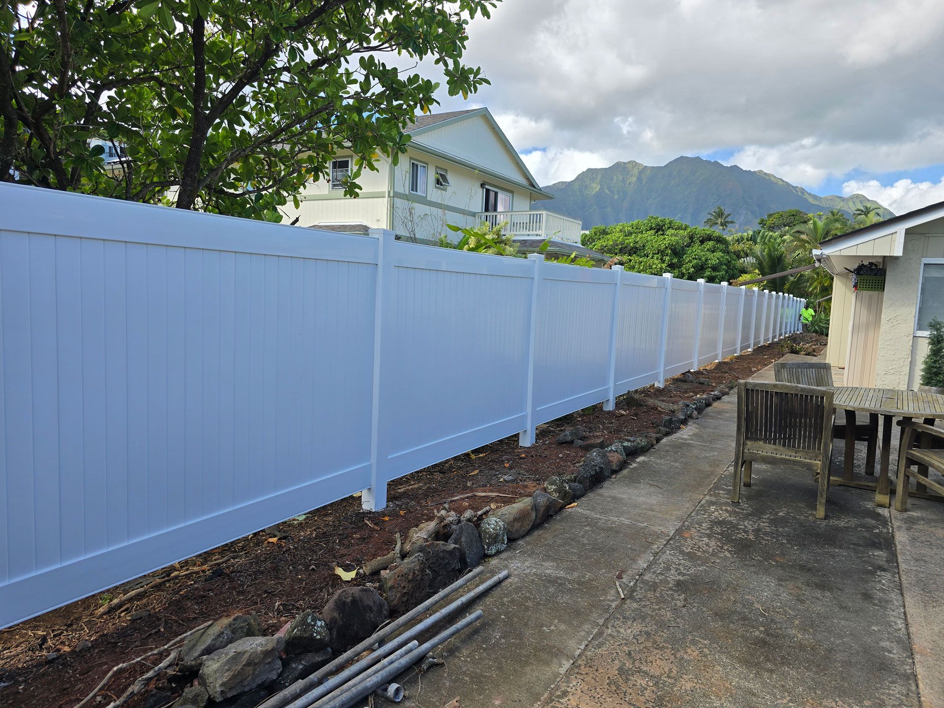 White vinyl fence along a walkway, with a house and mountains in the background.
