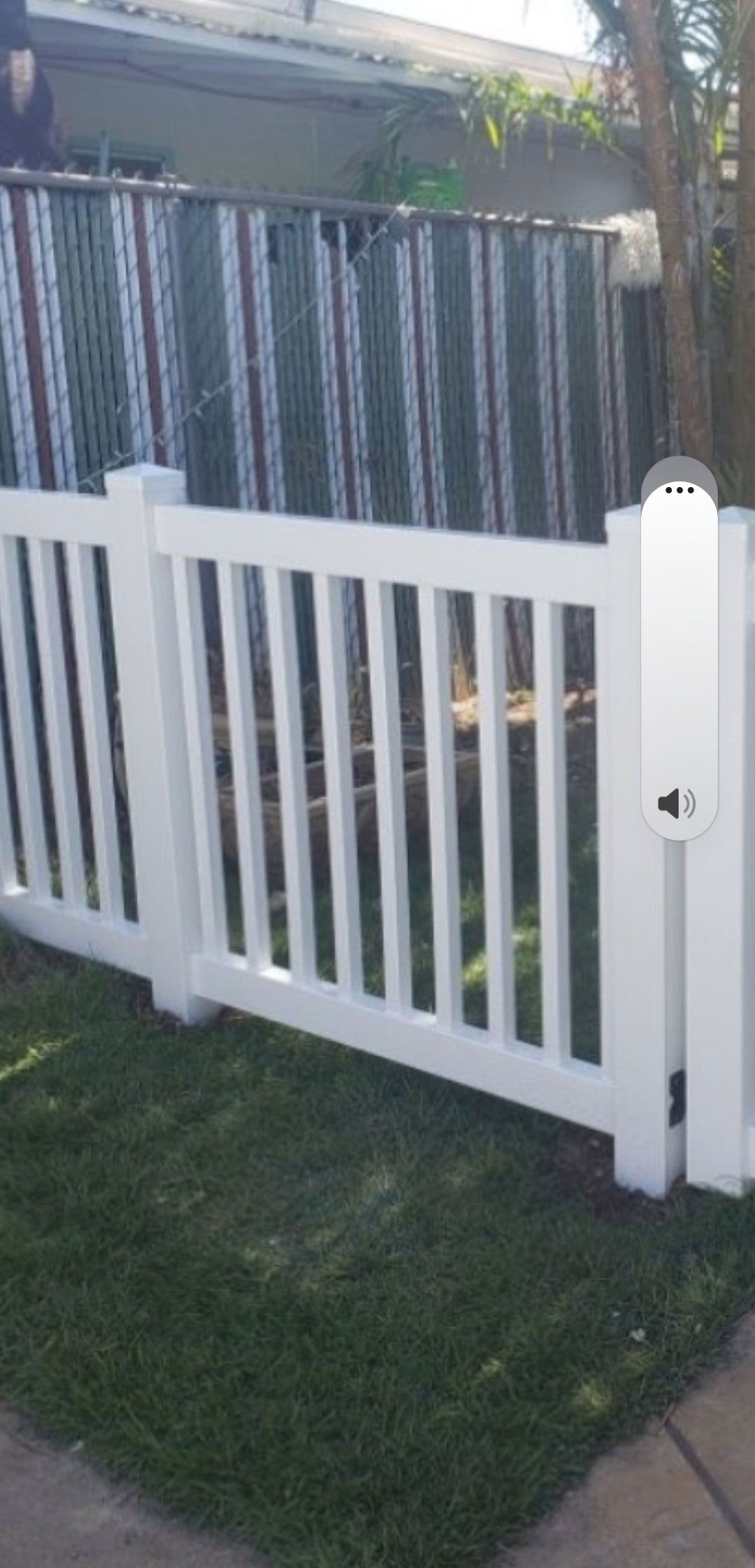 White picket fence with a gate, green grass, and a striped privacy fence.