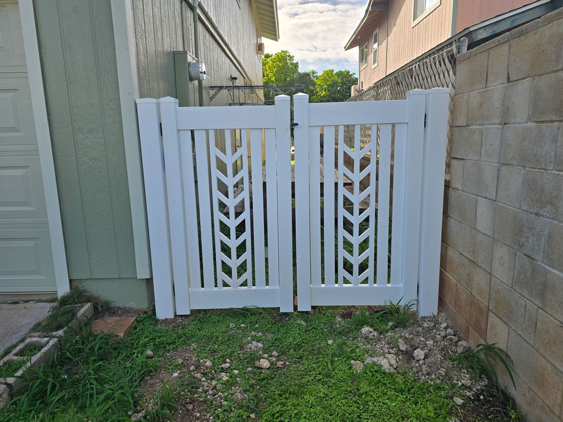 White double gate with a decorative wheat design, between a beige house and a cinder block wall.