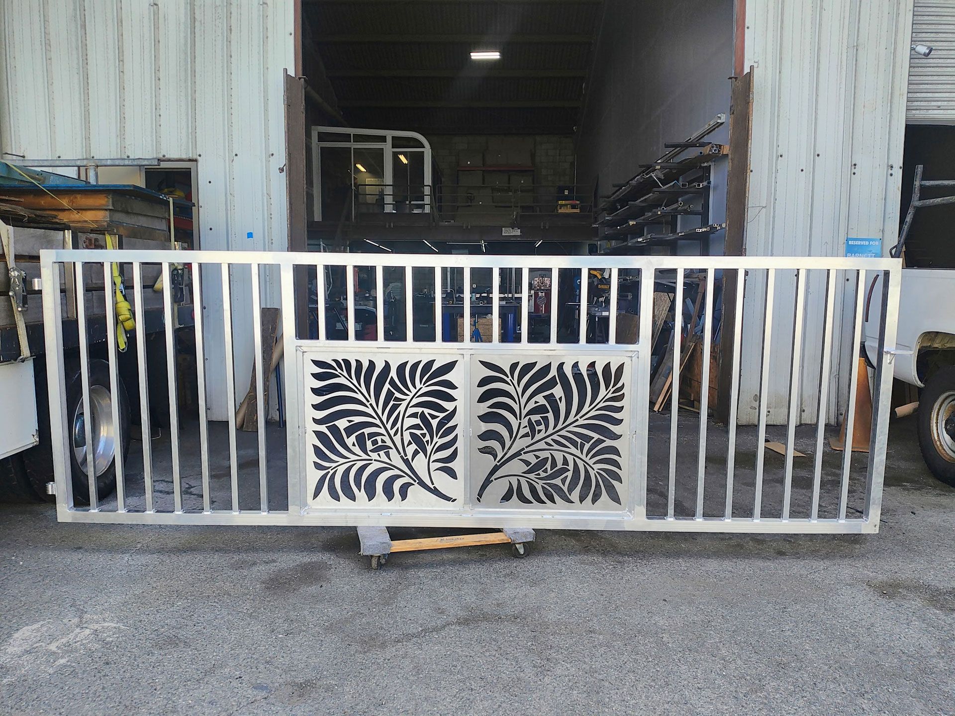 Silver metal gate with leaf design panels and vertical bars. Outdoors, in front of a building.