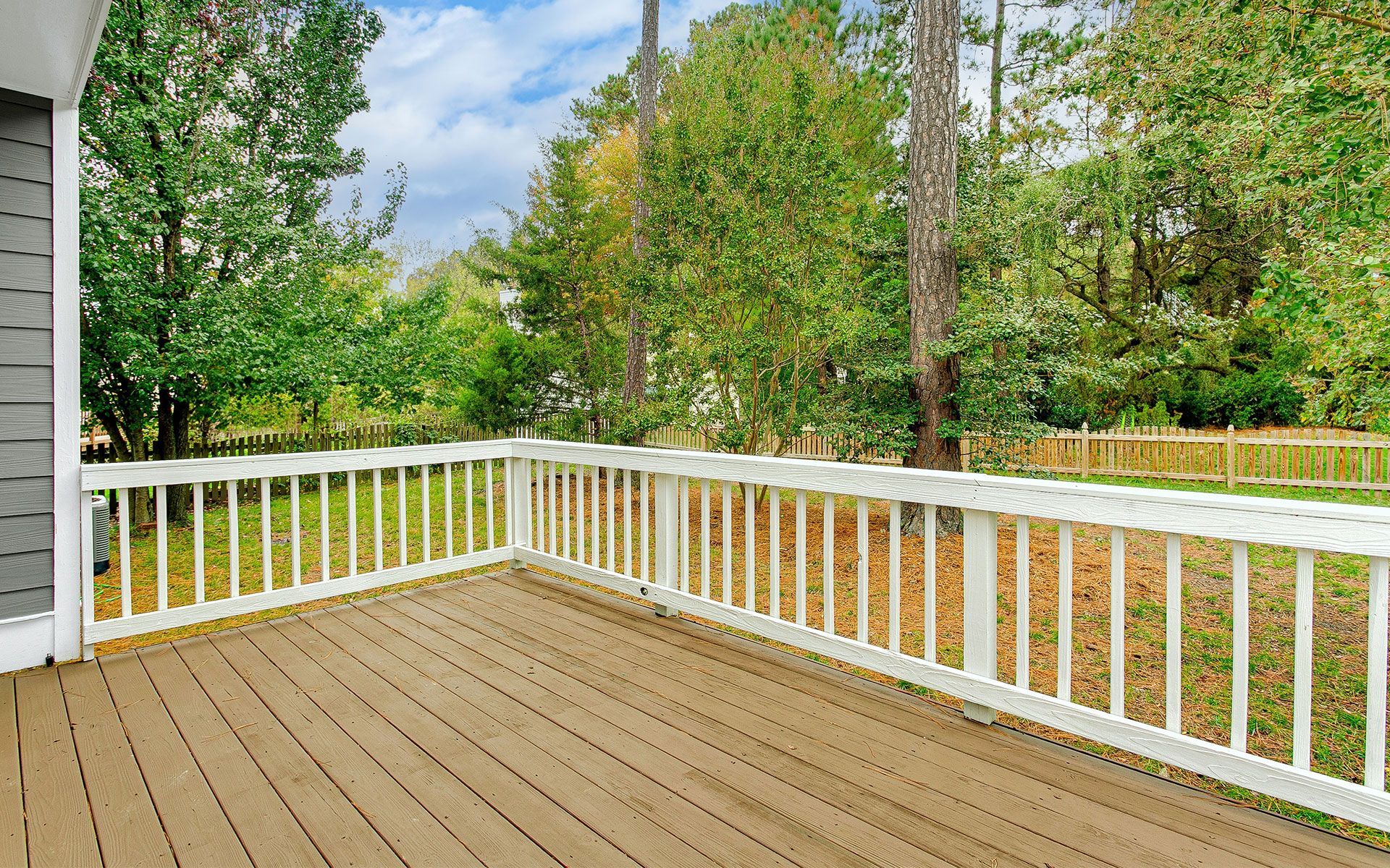 An empty deck with a white railing and trees in the background.