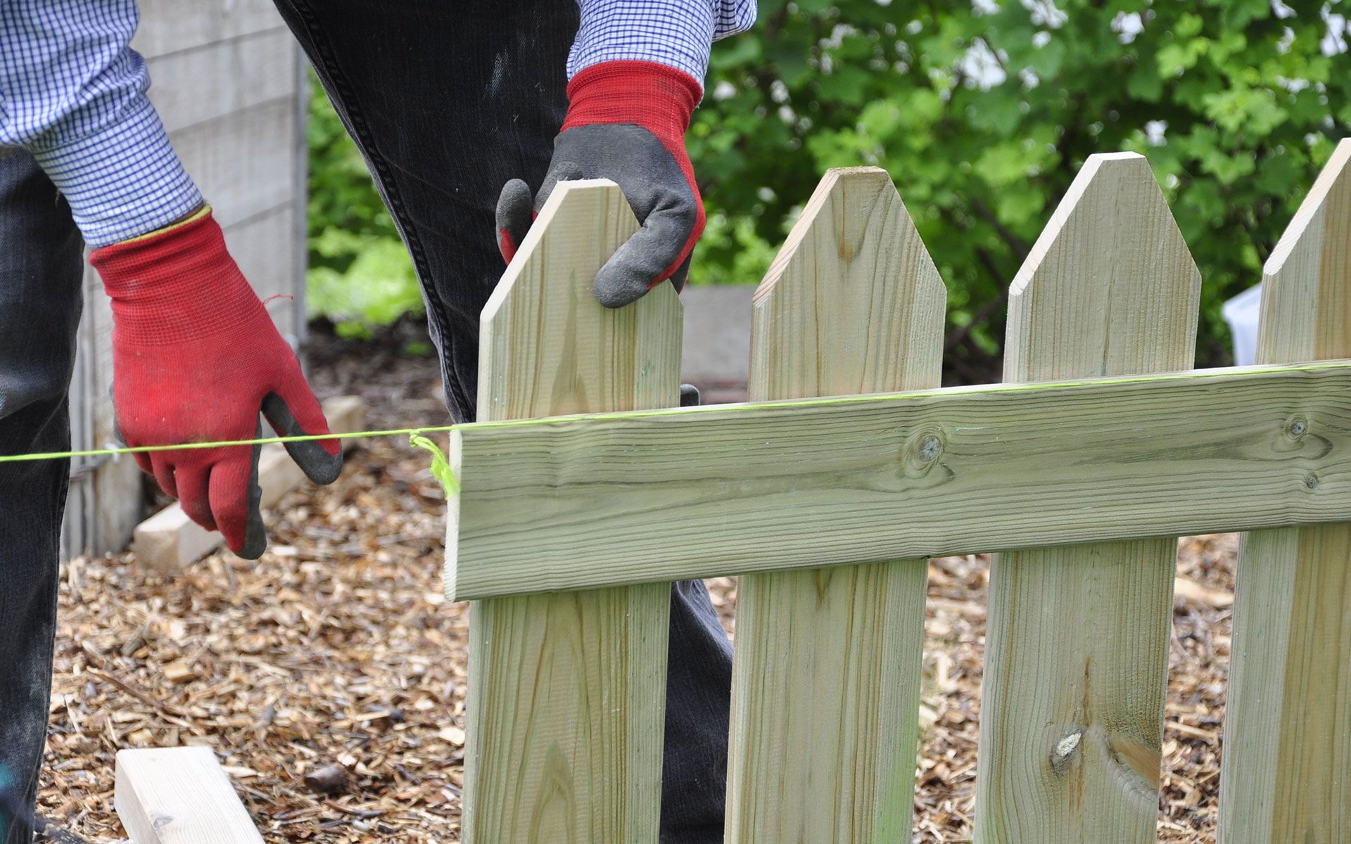 A person is measuring a wooden fence with a tape measure.