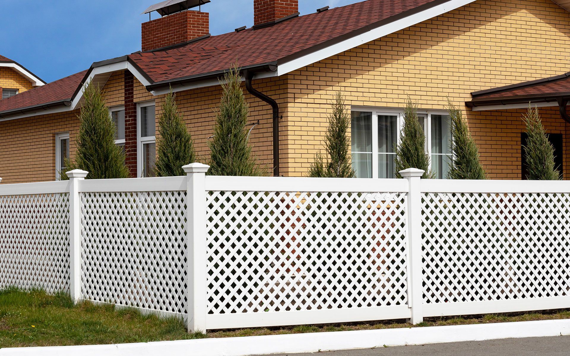 A white lattice fence is in front of a brick house.