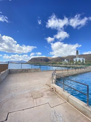 A concrete walkway leading to a body of water with mountains in the background.