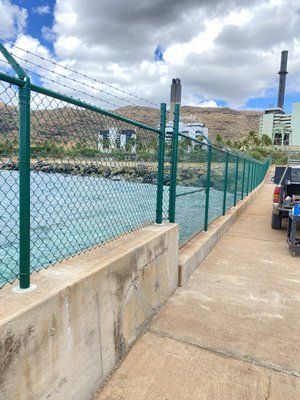 A chain link fence along a sidewalk next to a body of water.