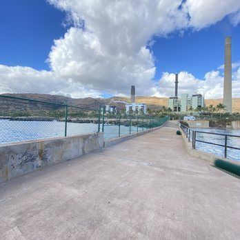 A concrete walkway leading to a large body of water with a power plant in the background.