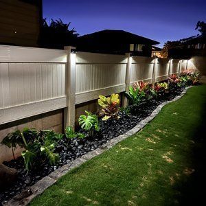 A white fence is surrounded by plants and rocks and is lit up at night.