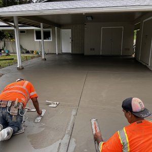 Two men are working on a concrete driveway in front of a house.