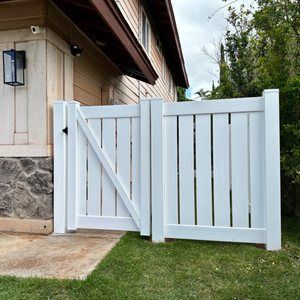 A white fence with a gate is in front of a house.