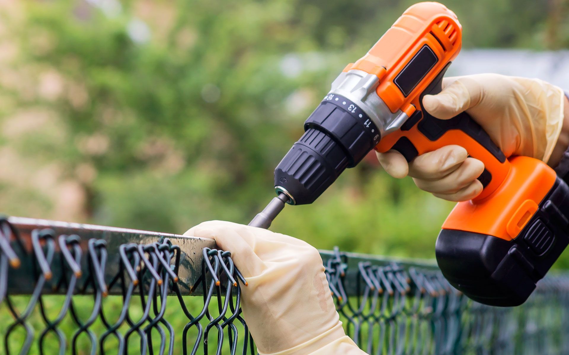 A person is using a drill to fix a chain link fence.