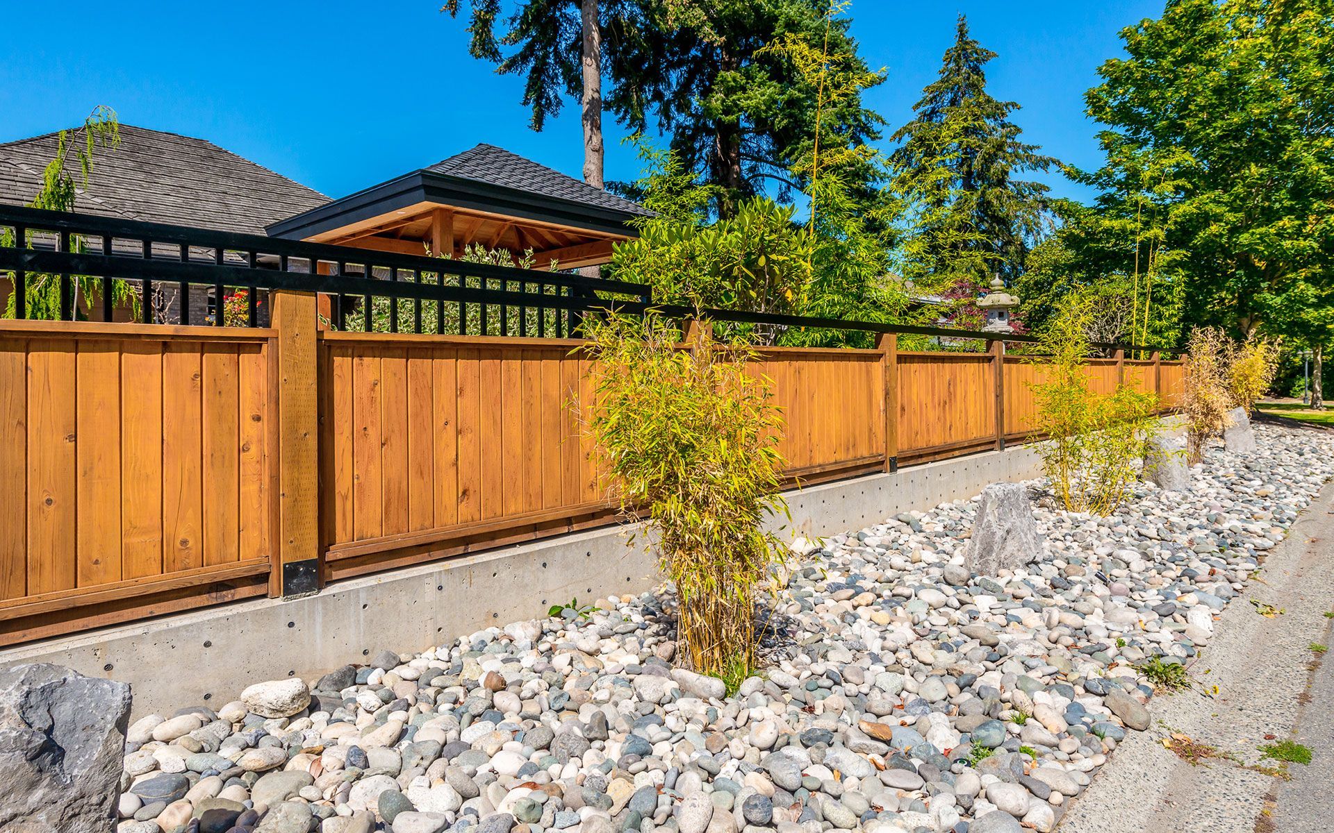 A wooden fence surrounds a rocky area in front of a house.