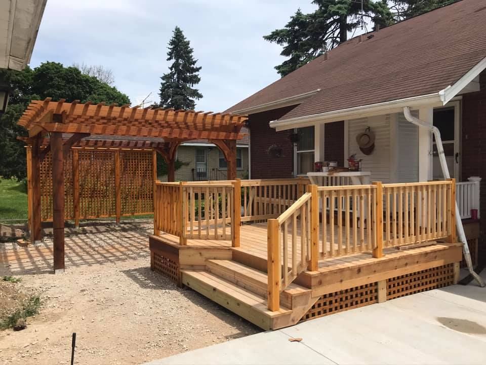 A wooden deck with stairs and a pergola in front of a house.