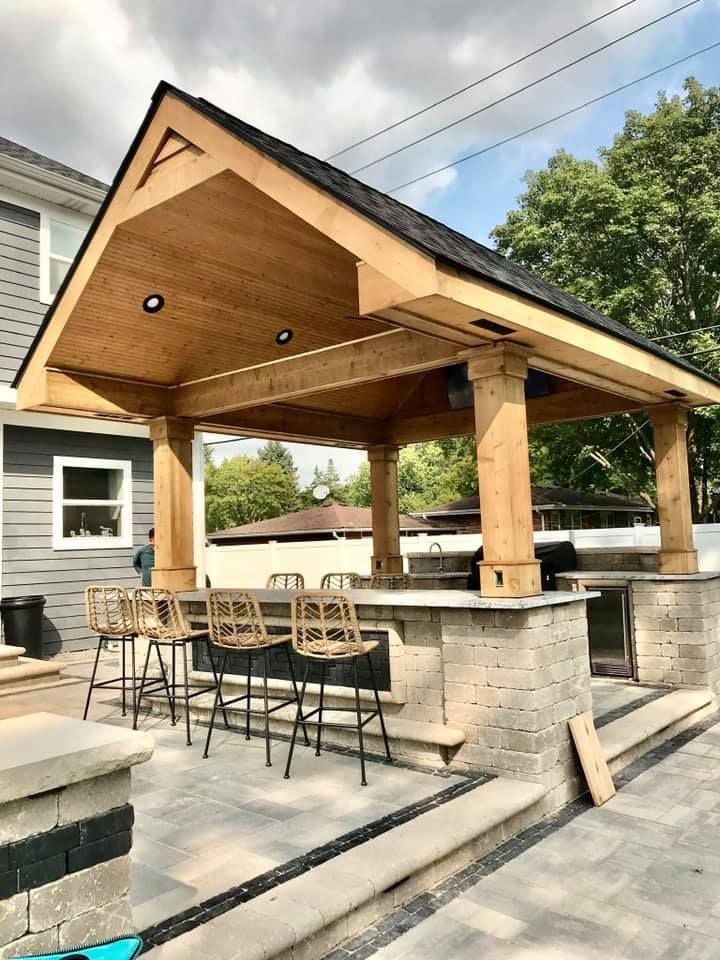 A wooden gazebo with a bar and stools in front of a house.