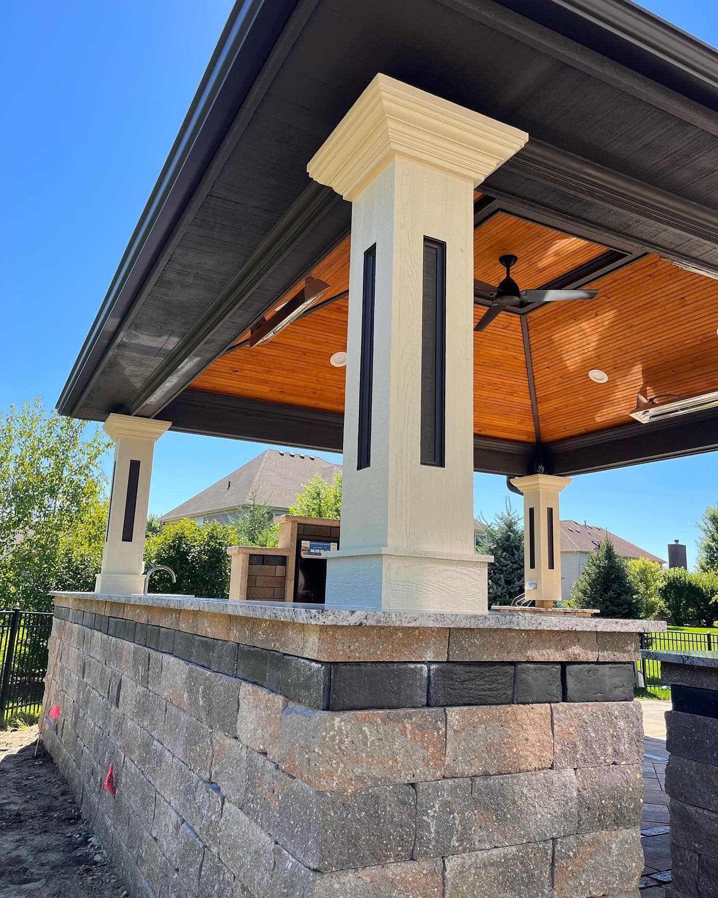 A gazebo with a ceiling fan and a brick wall underneath it.