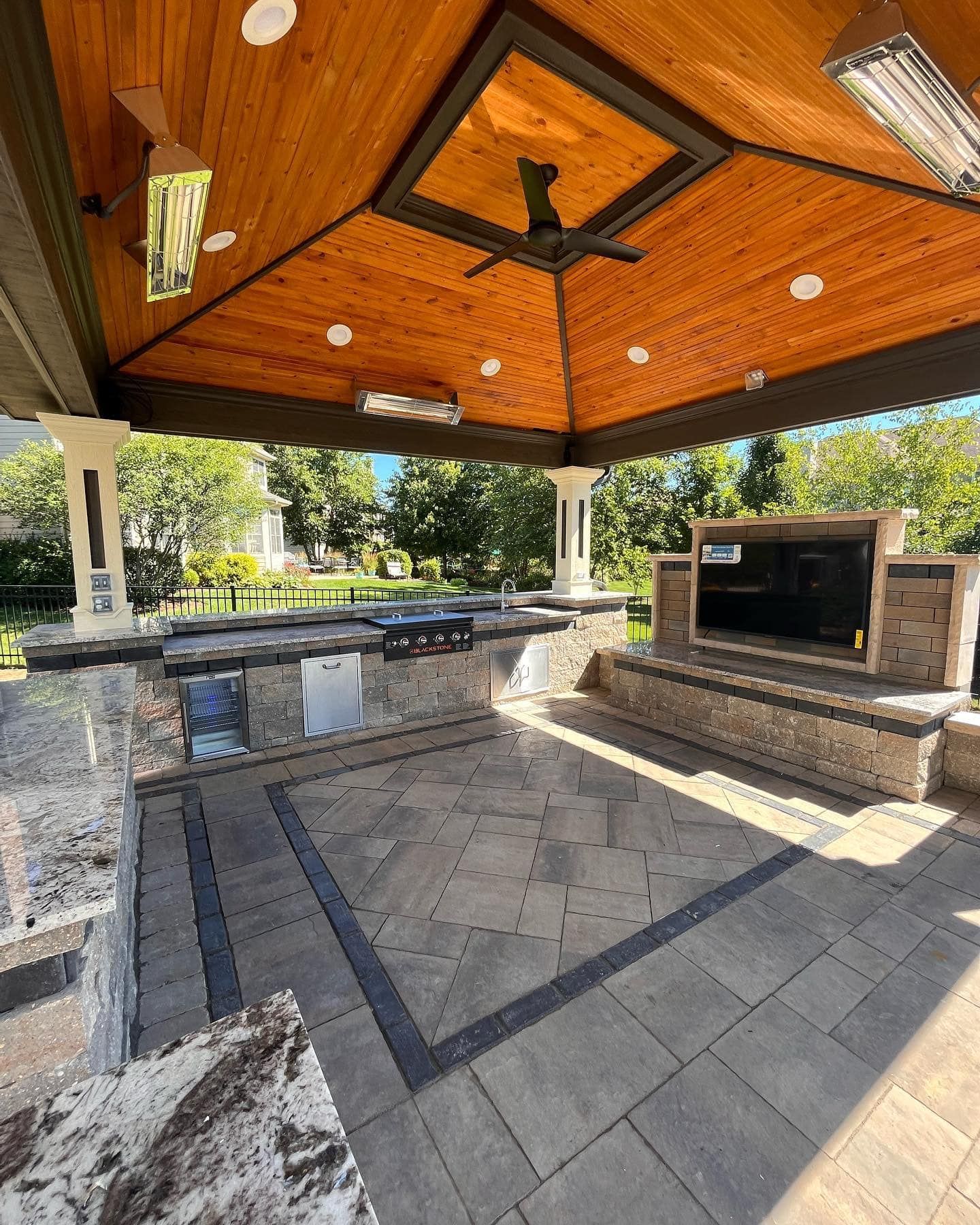 A large outdoor kitchen with a wooden ceiling and a ceiling fan.