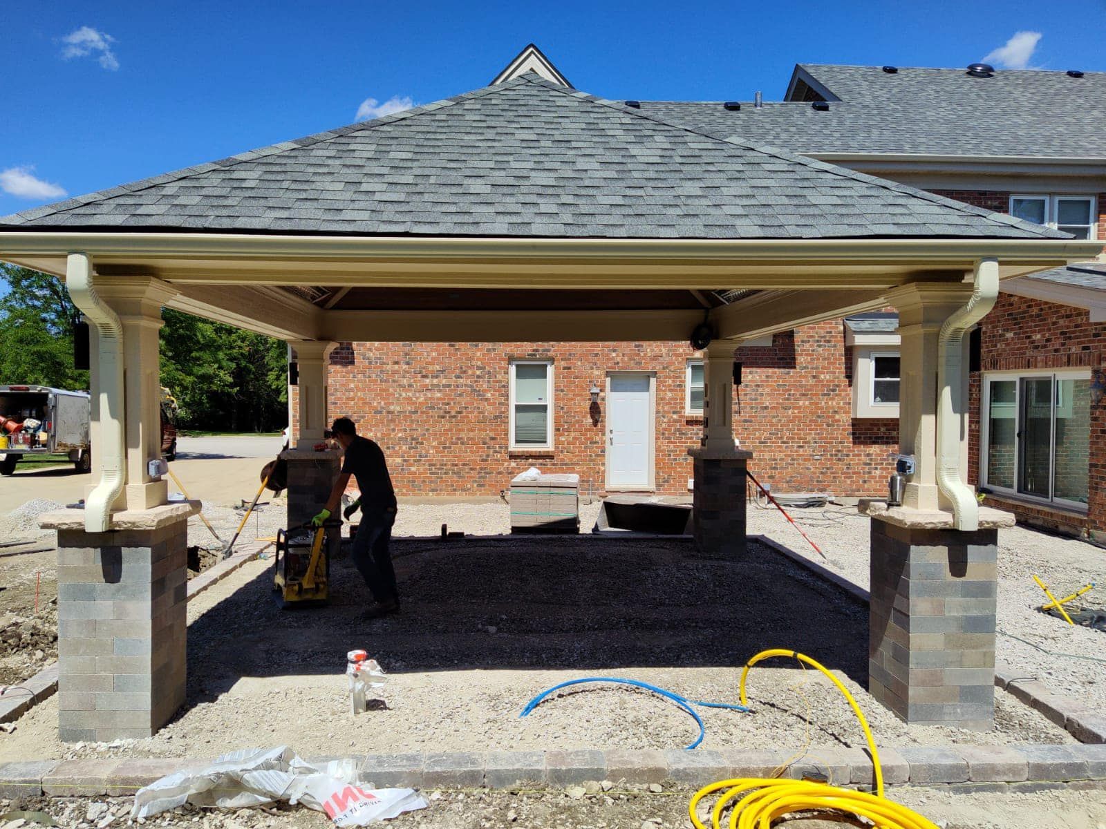 A man is working on a pavilion in front of a brick house.